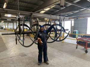 A worker in safety gear stands in a large industrial facility, holding onto a suspended metal auger—essential for Efficient Mixing processes with ISC Ribbon Mixers.