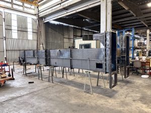 Large metal structure under construction, supported by two sawhorses, showcases ISC's expertise in vertical conveying systems like bucket elevators inside an industrial warehouse with tools and equipment visible in the background.