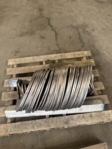 A stack of metal rings arranged on a wooden pallet in an industrial setting with a concrete floor, typically used in the manufacturing of custom screw conveyors by ISC.