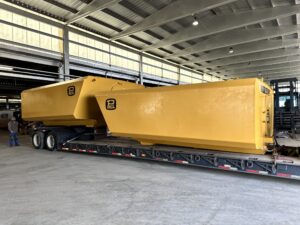 Two large yellow industrial components, a testament to over 50 years of manufacturing expertise at ISC Manufacturing, sit on a flatbed trailer inside a warehouse, with a person standing nearby.